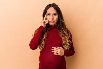 Young mexican pregnant woman isolated on beige background pointing temple with finger, thinking, focused on a task.