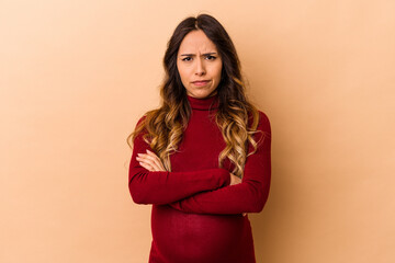 Fototapeta premium Young mexican pregnant woman isolated on beige background frowning face in displeasure, keeps arms folded.