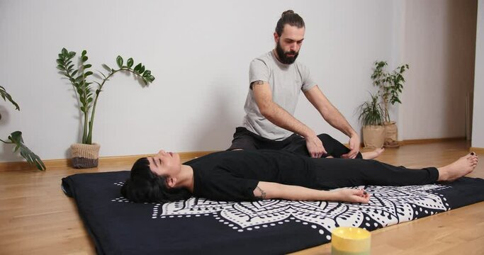 Mixed race latin woman having massage at home. Bearded man making yoga thai massage trigger point work shiatsu physical therapy fascia release