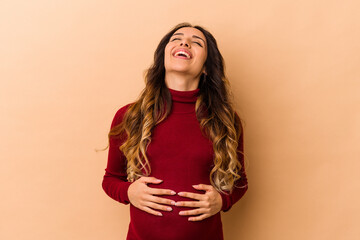 Young mexican pregnant woman isolated on beige background relaxed and happy laughing, neck stretched showing teeth.