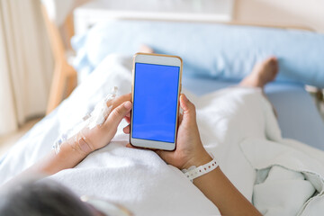 Health care technology concept, Blue Screen Mock up smartphone for Text, Hospital Patients woman senior using smart phone while Recovering moment whit saline, Iv drip, intravenous needle in Hospital