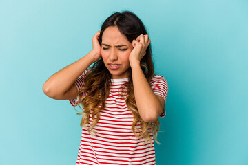 Young mexican woman isolated on blue background covering ears with hands.