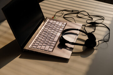 Headphones lie on a laptop keyboard on a white table. The shadow from the blinds falls on the desktop.