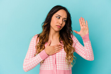 Young mexican woman isolated on blue background taking an oath, putting hand on chest.