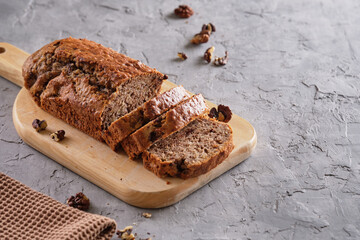 Delicious and flavorful banana cake with nuts and chocolate on a wooden board with a cup of coffee on a gray background