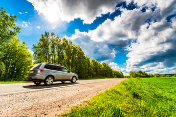 Car goes on the sunlit road through fields and forests. View from the side of the road