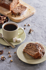 Delicious and flavorful banana cake with nuts and chocolate on a wooden board with a cup of coffee on a gray background