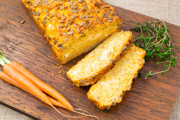 Carrot and thyme loaf on wooden board with fresh baby carrots and fresh thyme sprigs
