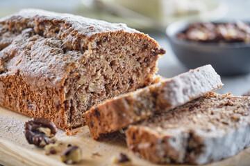Delicious and flavorful banana cake with nuts and chocolate on a wooden board with a cup of coffee on a gray background