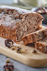 Delicious and flavorful banana cake with nuts and chocolate on a wooden board with a cup of coffee on a gray background