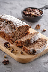 Delicious and flavorful banana cake with nuts and chocolate on a wooden board with a cup of coffee on a gray background