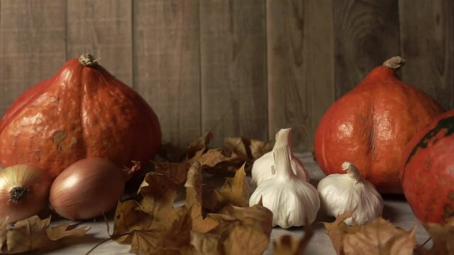 Still-life with autumn harvest and falling foliage in slowmo on wooden background. Agrarian composition made of pumpkins and onion with garlic surrounded by maple leaves. Farm decoration with raw food
