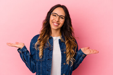 Young mexican woman isolated on pink background makes scale with arms, feels happy and confident.