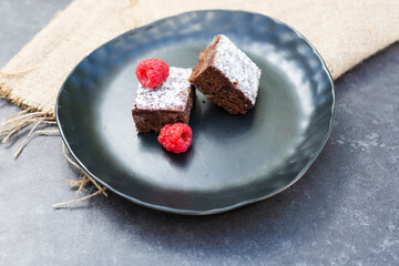 Two brownie slices on plate with two raspberries