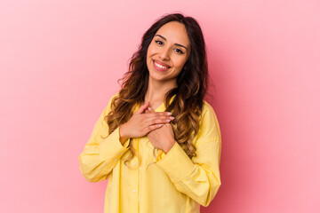 Young mexican woman isolated on pink background has friendly expression, pressing palm to chest. Love concept.