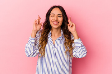 Young mexican woman isolated on pink background crossing fingers for having luck