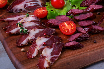 Jerked maral red deer meat and sausage served on the wooden board with cherry tomatoes and herbs. Venison delicacy 