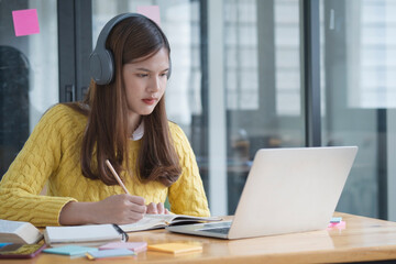Student wearing headphones using laptop studying at home, making research on laptop and browse internet, watching online webinar, listening audio course, e-learning education concept