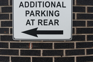 black text on white ground sign that reads: additional parking at rear with a black arrow pointing left