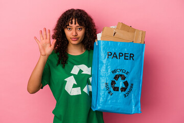 Young caucasian woman holding a recycled plastic isolated on pink background smiling cheerful showing number five with fingers.