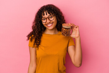 Young mixed race woman holding an almond jar isolated on pink background happy, smiling and cheerful.