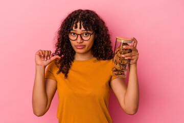 Young mixed race woman holding a cookies jar isolated on pink background showing a dislike gesture,...