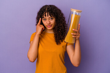 Young mixed race woman holding spaghetti isolated on purple background pointing temple with finger, thinking, focused on a task.