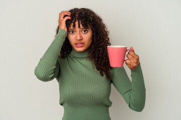 Young mixed race woman holding a mug isolated on white background being shocked, she has remembered important meeting.