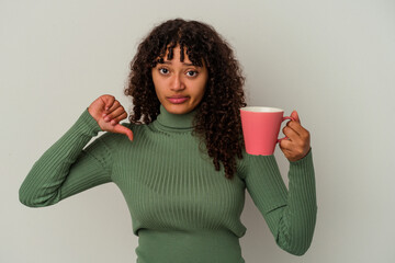 Young mixed race woman holding a mug isolated on white background showing a dislike gesture, thumbs...
