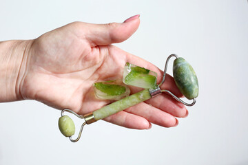 Hand holding green face roller and ice cubes. Derma roller for skin care.