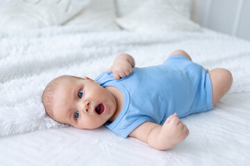 yawning baby boy three months old in a blue bodysuit on a white bed at home goes to bed
