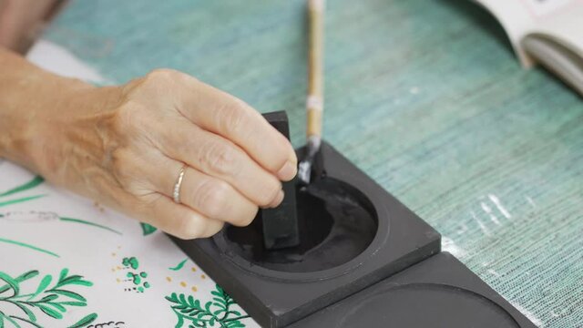 close up hand of senior woman grinding ink stick on ink stone before paint Chinese calligraphy