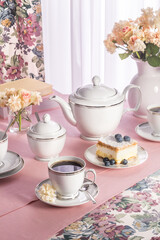 A photo of a set of white porcelain on a pink tablecloth in a composition with flowers