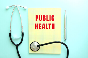 The red text PUBLIC HEALTH is written in a yellow pad that lies next to the stethoscope on a blue...