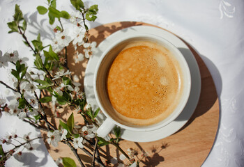 A cup of coffee, a book and blooming cherry branches on a white tablecloth. White sakura. Atmosphere, comfort, rest