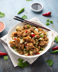 Stir fry chinese salt and pepper chicken with red, green chilli, onion, spring onion in white bowl.