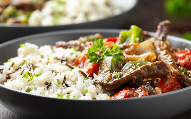 Stir fry Chinese pepper beef steak with onion, red and green bell pepper, rice in bowl