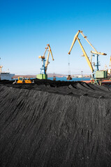 Huge amount of coal in the Murmansk commercial seaport. Loading of coal by buckets (grabs) of portal cranes into the holds of a dry cargo ship in the seaport