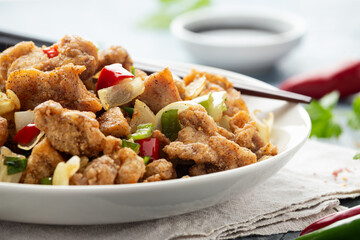 Stir fry chinese salt and pepper chicken with red, green chilli, onion, spring onion in white bowl.
