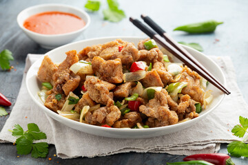 Stir fry chinese salt and pepper chicken with red, green chilli, onion, spring onion in white bowl.