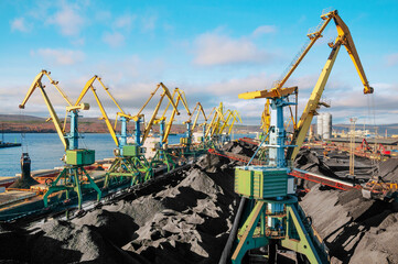 Huge amount of coal in the Murmansk commercial seaport. Loading of coal by buckets (grabs) of portal cranes into the holds of a dry cargo ship in the seaport