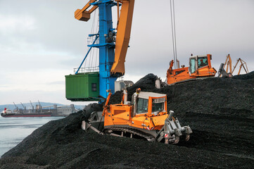 Bulldozers are shoveling coal. Piles of coal in the commercial seaport for further transportation by sea dry cargo ships