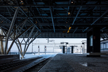 Fototapeta premium An empty railway station platform, looking out at the snow-covered railroad tracks