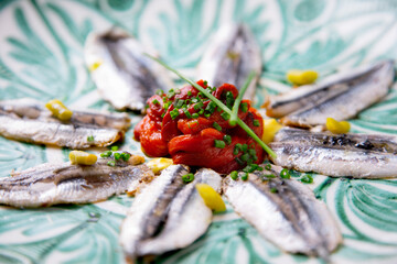 Fototapeta na wymiar Plate of anchovies with roasted peppers and piparras. Traditional Spanish tapa served on a plate of the Andalusian culture.