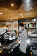 A masked barista prepares delicious coffee at the bar in a cafe. The work of restaurants and cafes during the pandemic.