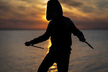 boy posing like assassin in the sunset silhuette orange colors