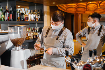 Two masked baristas prepare delicious coffee in the cafe bar. The work of restaurants and cafes during the pandemic.