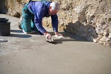 The mason on his knees coats the concrete floor with cement