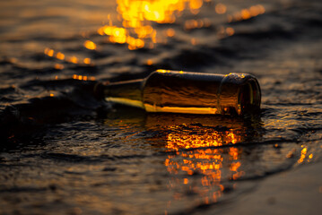 Overturned beer bottle in sunset sea water with bokeh in the background and glare in the water.