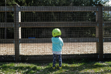 A girl stop by the fence of a dog park with her bike helmet on